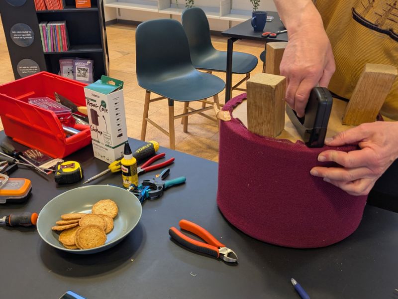 Mand betrækker skammel på et bord fyldt med værktøj