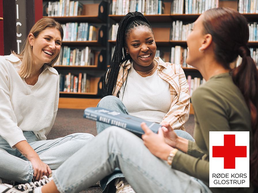 Tre unge kvinder i et bibliotek sidder på gulvet og taler sammen